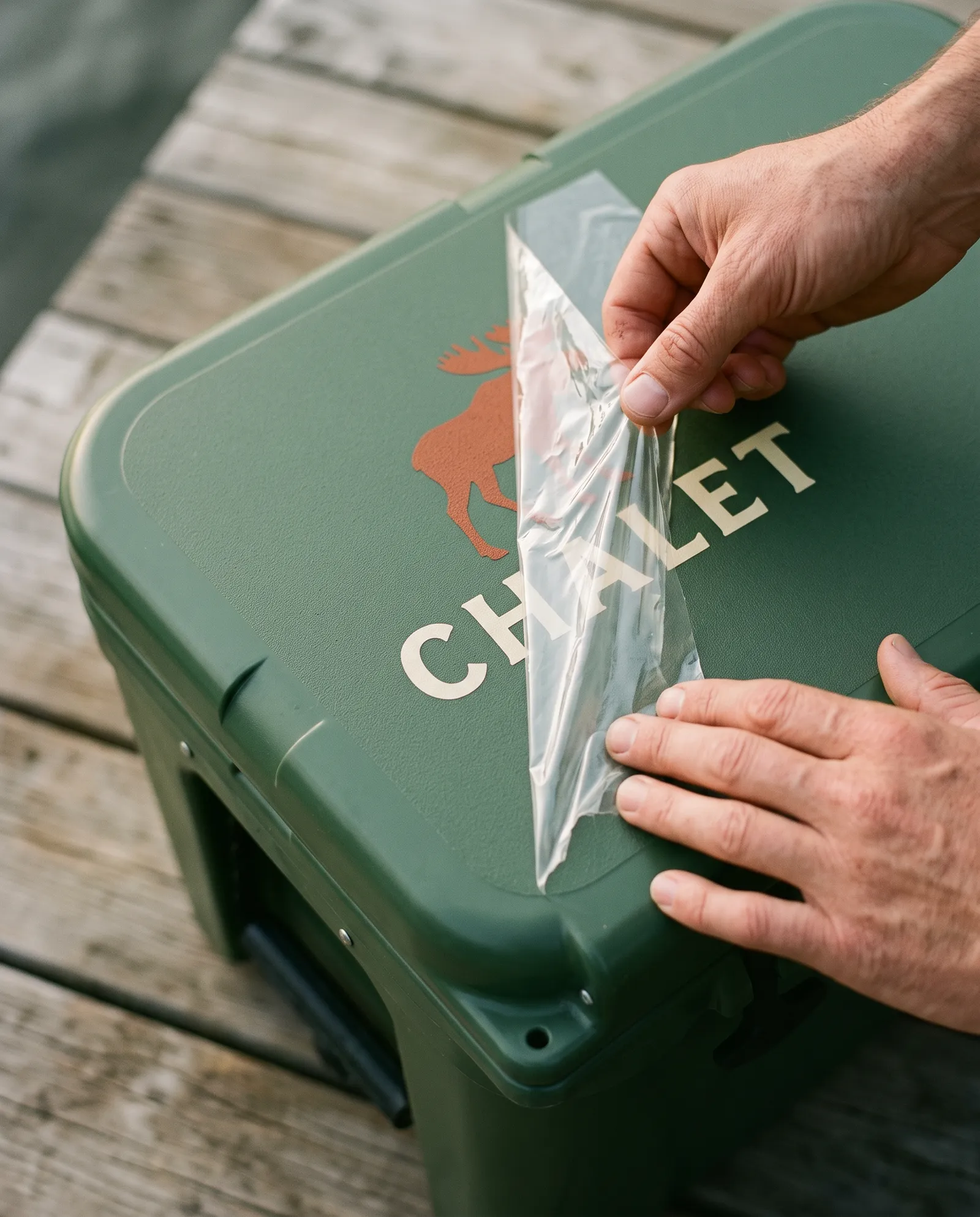 On retire le film transparent d'un transfert posé sur une glacière verte&nbsp;: il ne reste que l'orignal et le mot CHALET