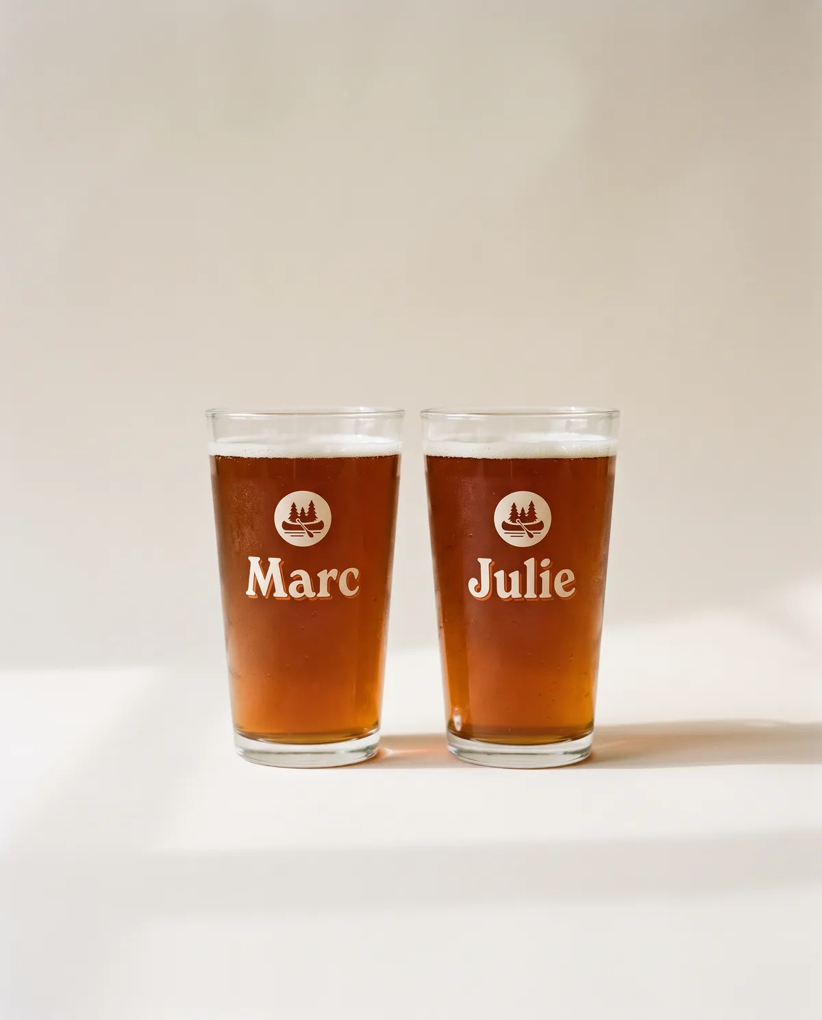 Deux verres de bière imprimés d'un écusson canot et épinettes, aux prénoms Marc et Julie